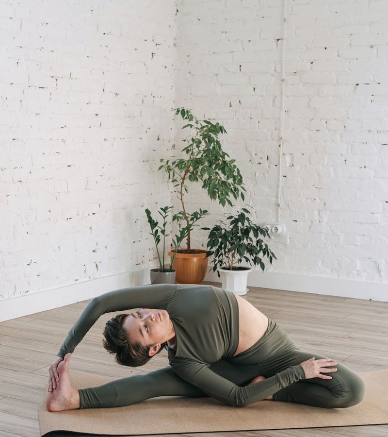 Woman in a calm yoga pose in a softly lit room with plants.